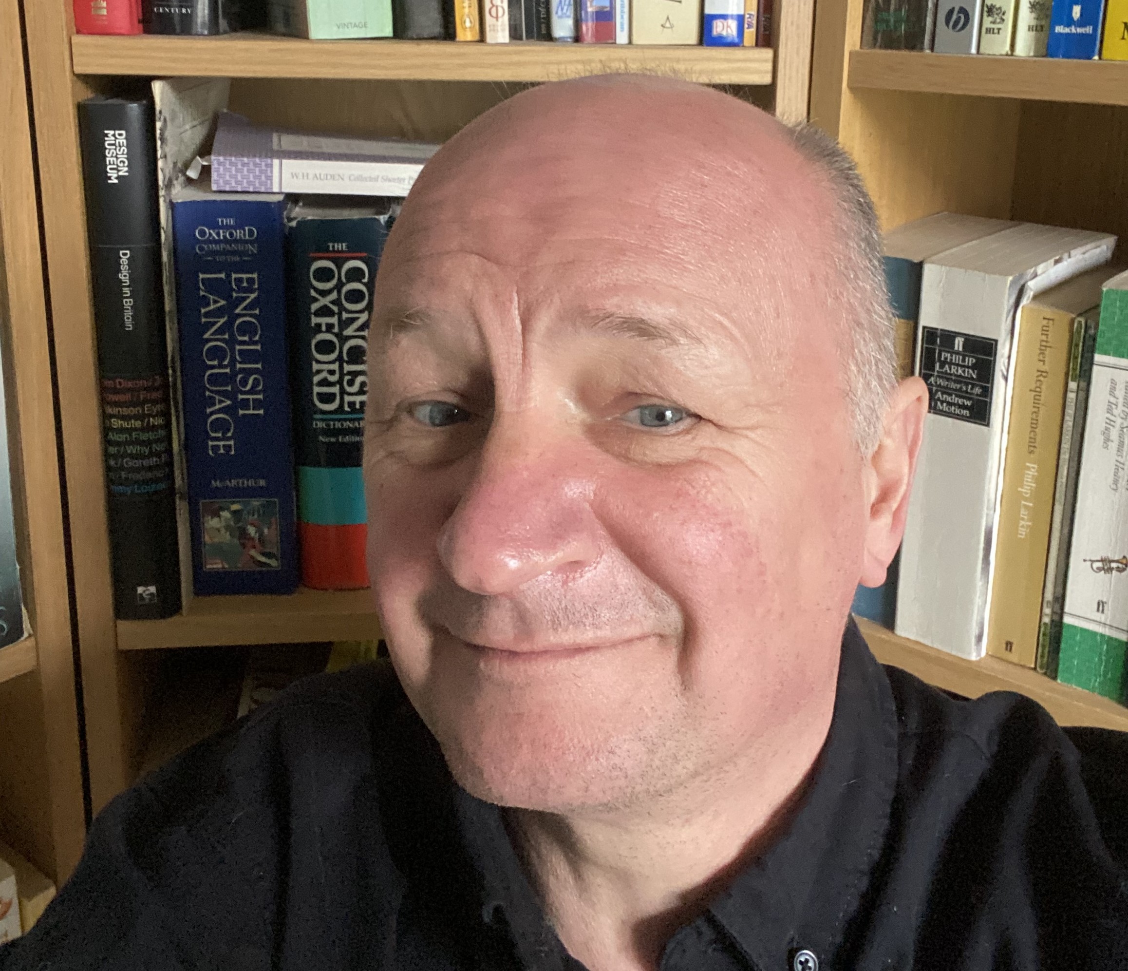 A selfie of an older man in front of a bookshelf