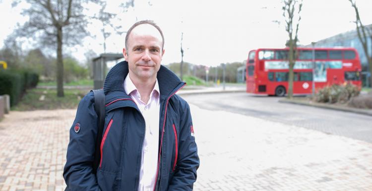 Person standing outside with London bus behind them