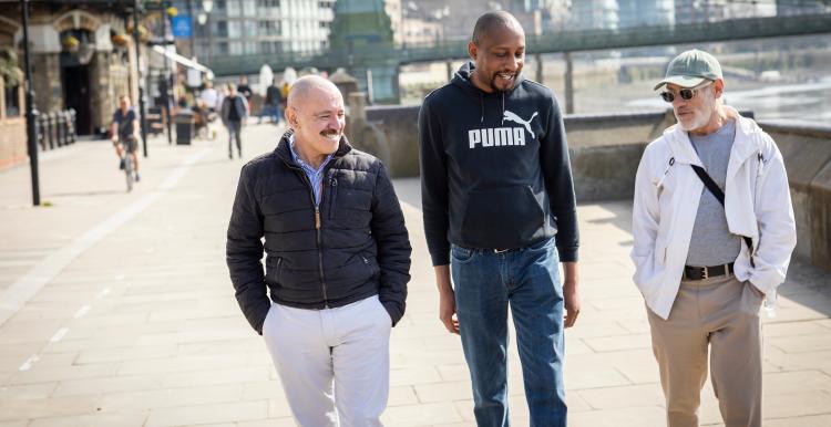 Three men walking together on footpath.
