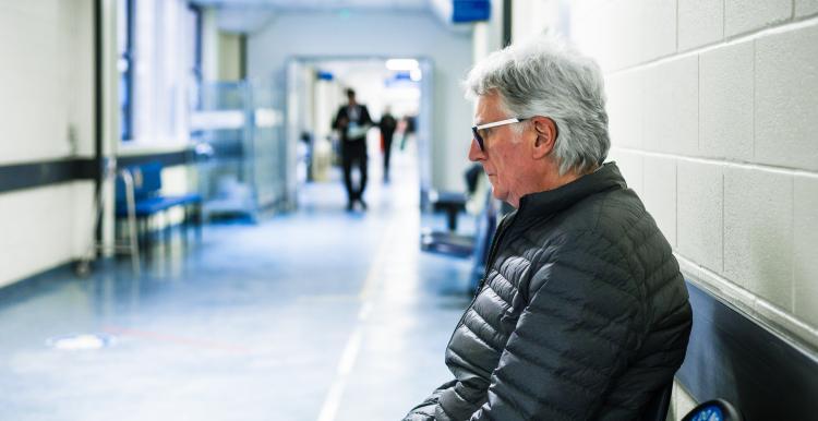 A man wearing glasses sitting on a bench and waiting at the hospital