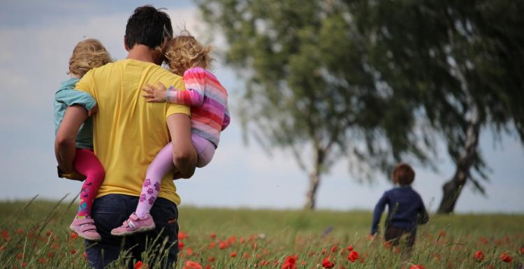 A man holding two young children walking in a poppy field along with another young girl