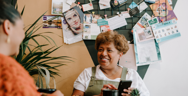 Lady smiling and holding a cup of coffee. Notice board behind her