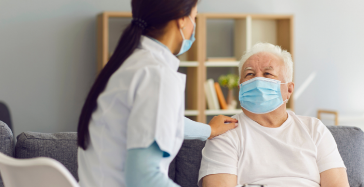 Older man in mask in care home with carer