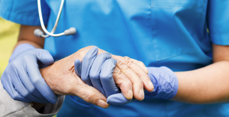 A healthcare worker holding the hand of an elderly person while wearing protective gloves