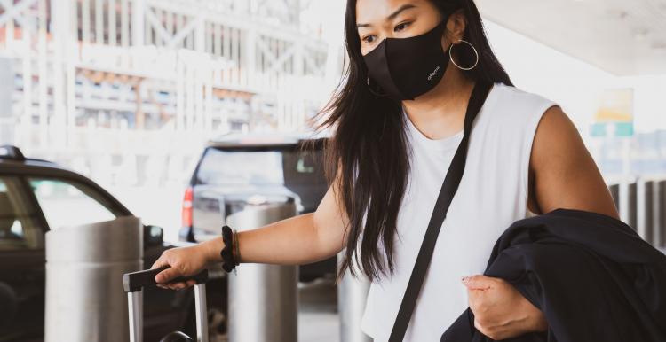 Young Asian woman wearing a face mask and holding carry on luggage outside an airport
