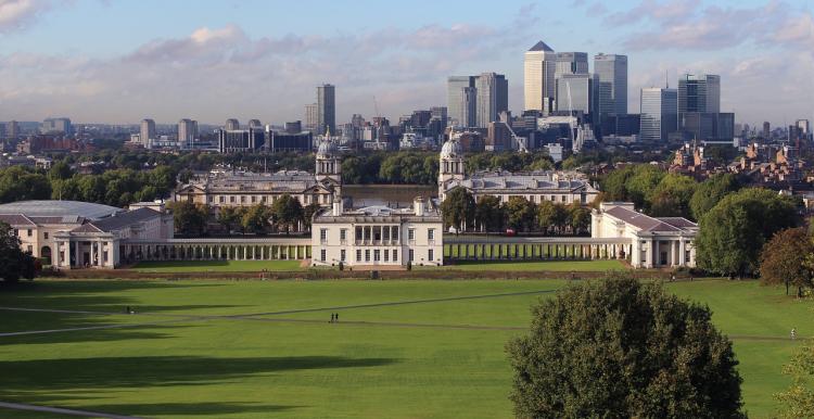 A photo of Greenwich park on a sunny day, taken from a hilltop facing the Royal Naval College and Canary Wharf