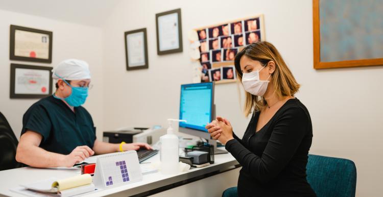 A patient using hand sanitiser in a consultation room and a GP wearing face masks