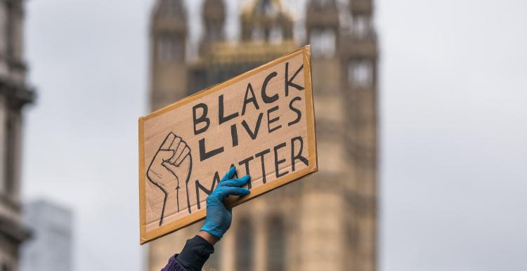 a protester holding up a "black lives matter" sign with the houses of parliament in the background