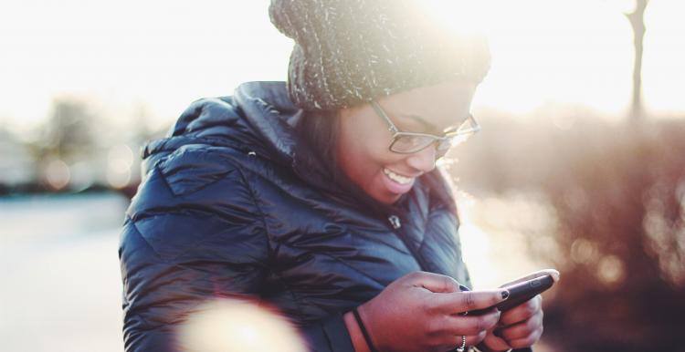 A smiling black woman looking at her smartphone standing at a park
