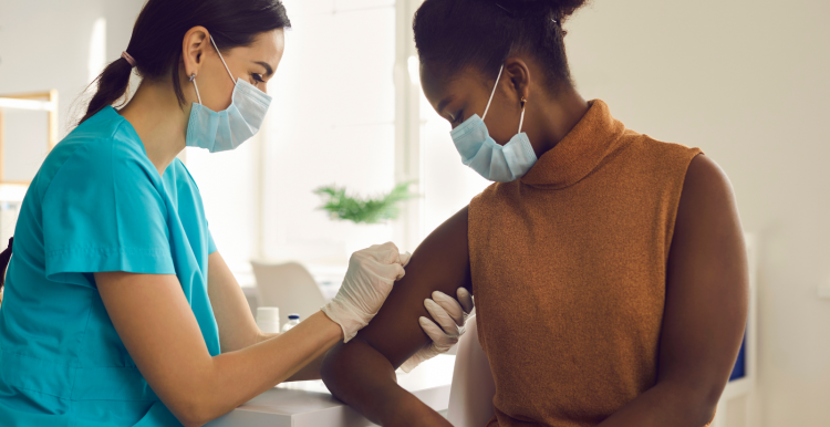 Woman being vaccinated by health professional in medical gloves in bright room