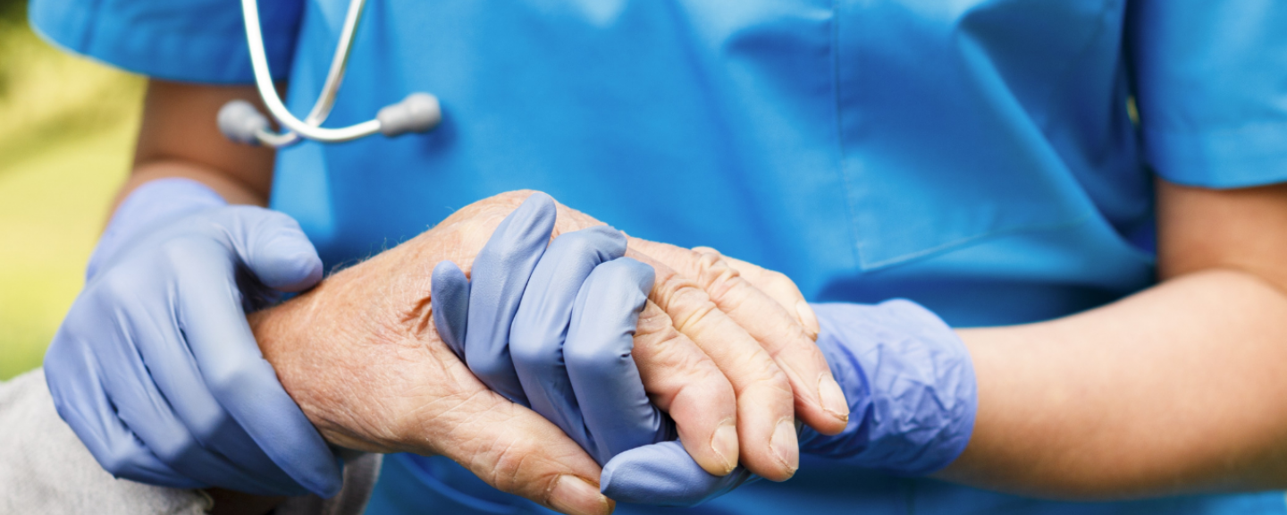 A healthcare worker holding the hand of an elderly person while wearing protective gloves