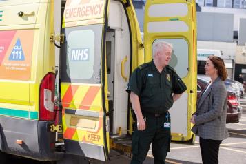 Ambulance driver standing behind an ambulance speaking to a woman.