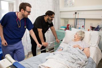 Patient in hospital bed speaking to two doctors.