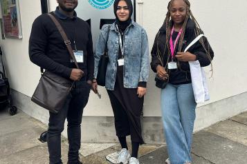 Three Healthwatch Greenwich volunteers standing in front of Woolwich Community Centre sign.