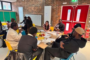 Young people seated around table speaking to Healthwatch Greenwich staff member.