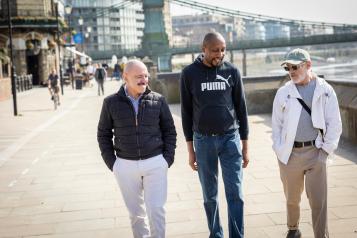Three men walking together on footpath.