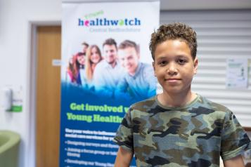 Young male volunteer standing in front of Healthwatch branding