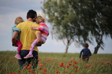A man holding two young children walking in a poppy field along with another young girl