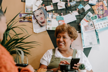 Lady smiling and holding a cup of coffee. Notice board behind her