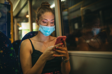 woman wearing mask on bus and looking at her phone