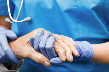 A healthcare worker holding the hand of an elderly person while wearing protective gloves