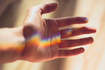 A hand gently spread out with a colourful light reflection going across it