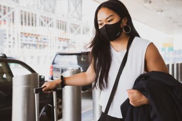 Young Asian woman wearing a face mask and holding carry on luggage outside an airport