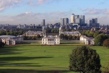 A photo of Greenwich park on a sunny day, taken from a hilltop facing the Royal Naval College and Canary Wharf