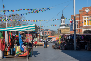 A man walking through colourful Woolwich market on a sunny day