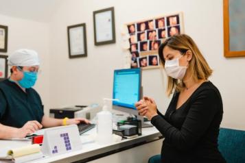 A patient using hand sanitiser in a consultation room and a GP wearing face masks