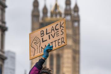 a protester holding up a "black lives matter" sign with the houses of parliament in the background