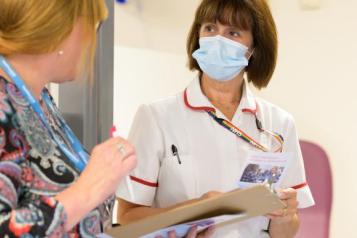 Two nurses wearing COVID face masks talk to each other