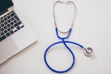 A blue stethoscope on a white desk next to a laptop