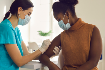 Woman being vaccinated by health professional in medical gloves in bright room