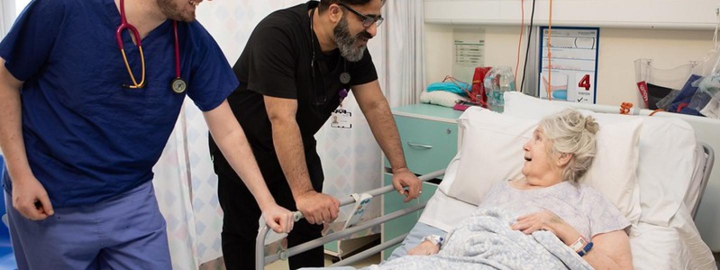 Patient in hospital bed speaking to two doctors.