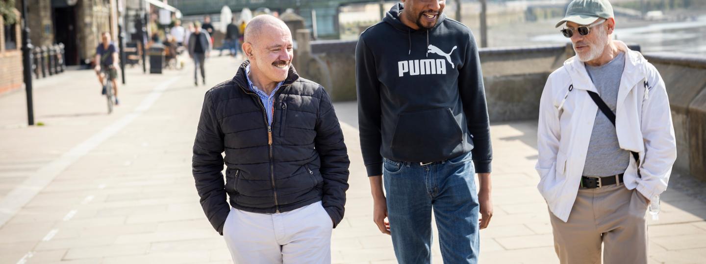 Three men walking together on footpath.