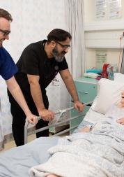 Patient in hospital bed speaking to two doctors.