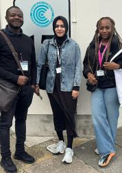 Three Healthwatch Greenwich volunteers standing in front of Woolwich Community Centre sign.