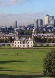 A photo of Greenwich park on a sunny day, taken from a hilltop facing the Royal Naval College and Canary Wharf