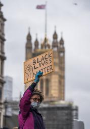 a protester holding up a "black lives matter" sign with the houses of parliament in the background
